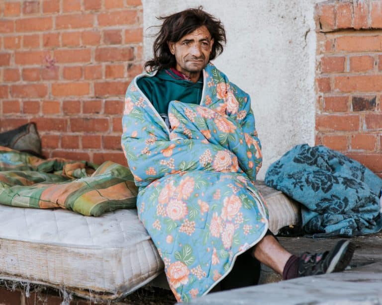 vista frontal de um morador de rua no colchao ao ar livre sob o cobertor